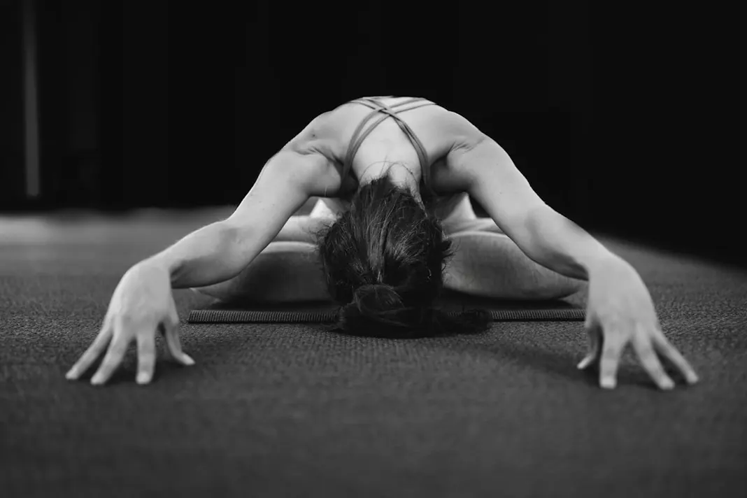 Black and white photo of a woman folding forward in a seated stretch on the floor