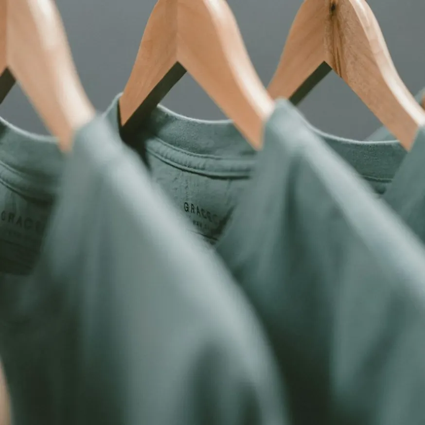 Close-up of sage green tops hanging on wooden hangers